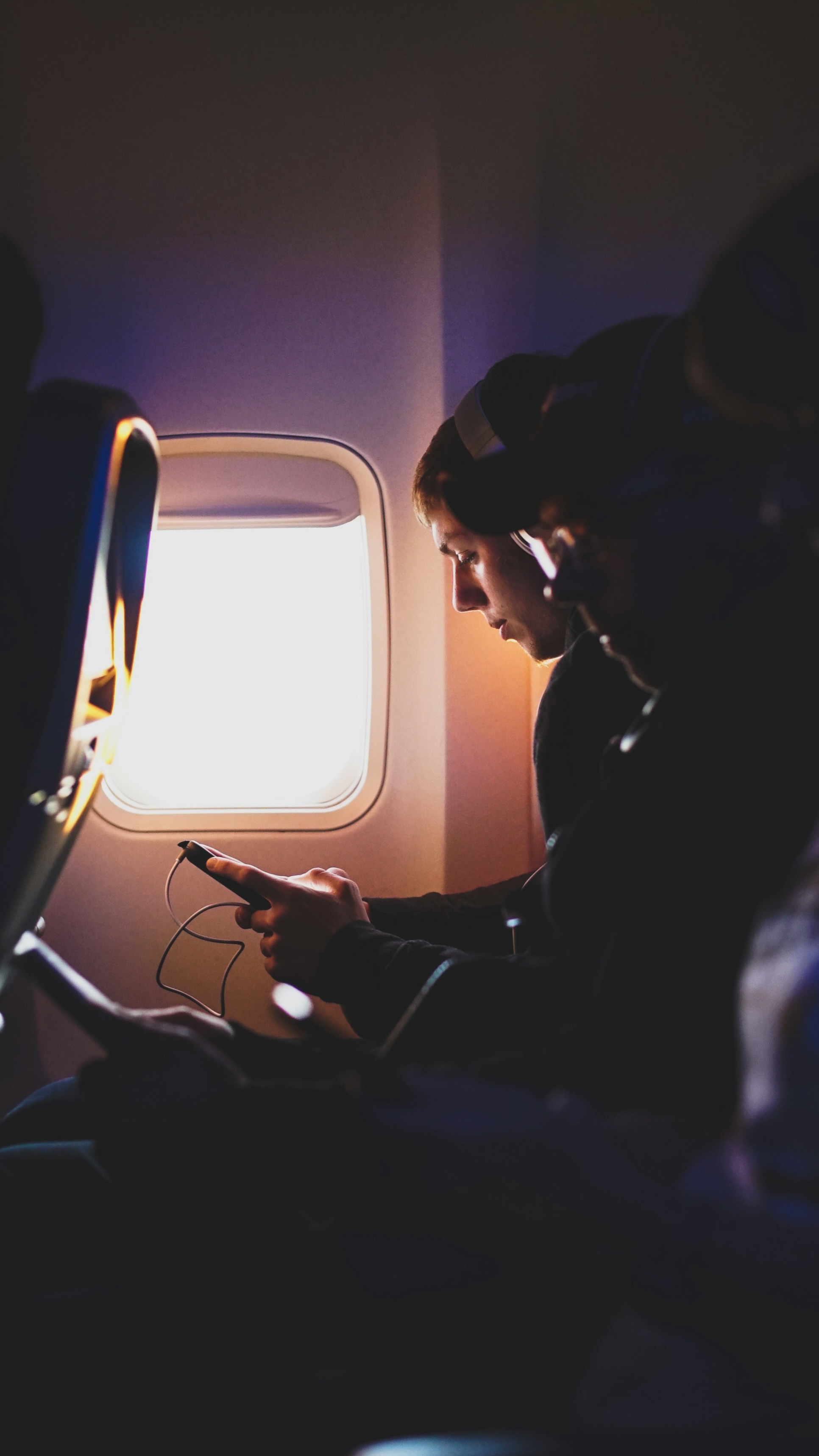 A passenger using a phone while wearing headphones on a plane.